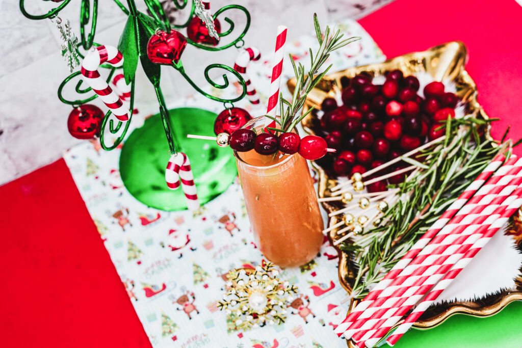 Christmas mimosas styled on a table with straws, fresh cranberries, rosemary, and more.