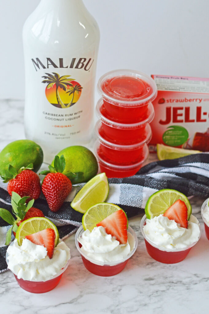 Strawberry Daiquiri Jello Shots on a table with fresh strawberries and limes