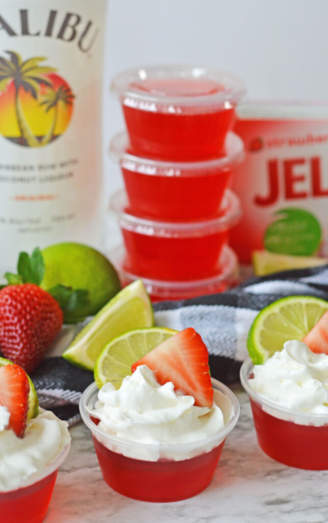 A Strawberry Daiquiri Jello Shot topped with whipped cream, a strawberry halve and a lime slice.