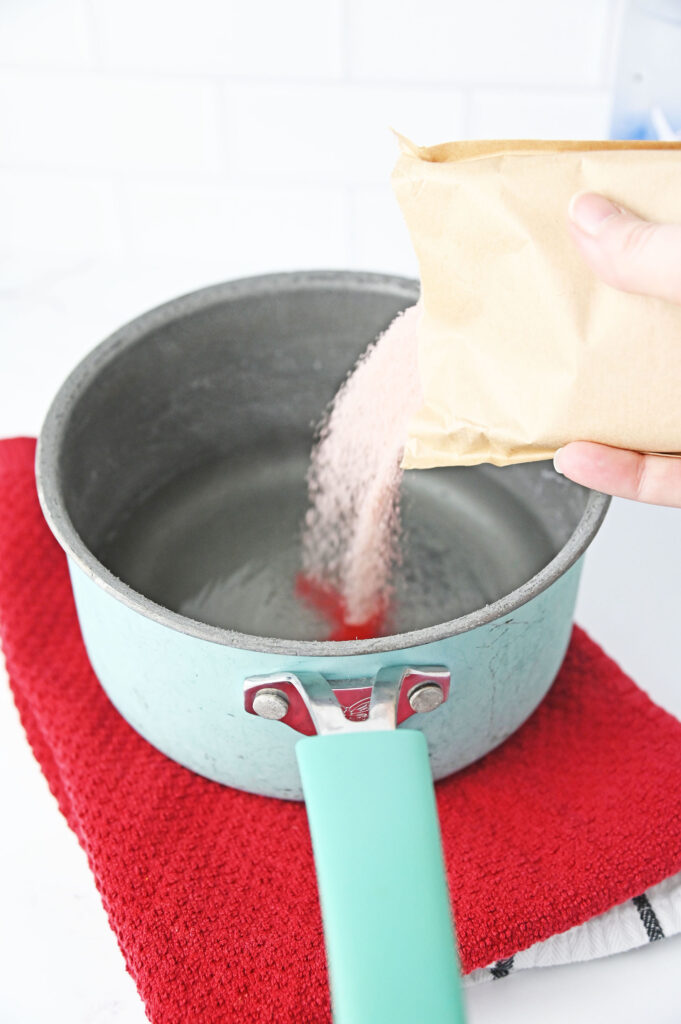 strawberry jello mix pouring into a pot of water