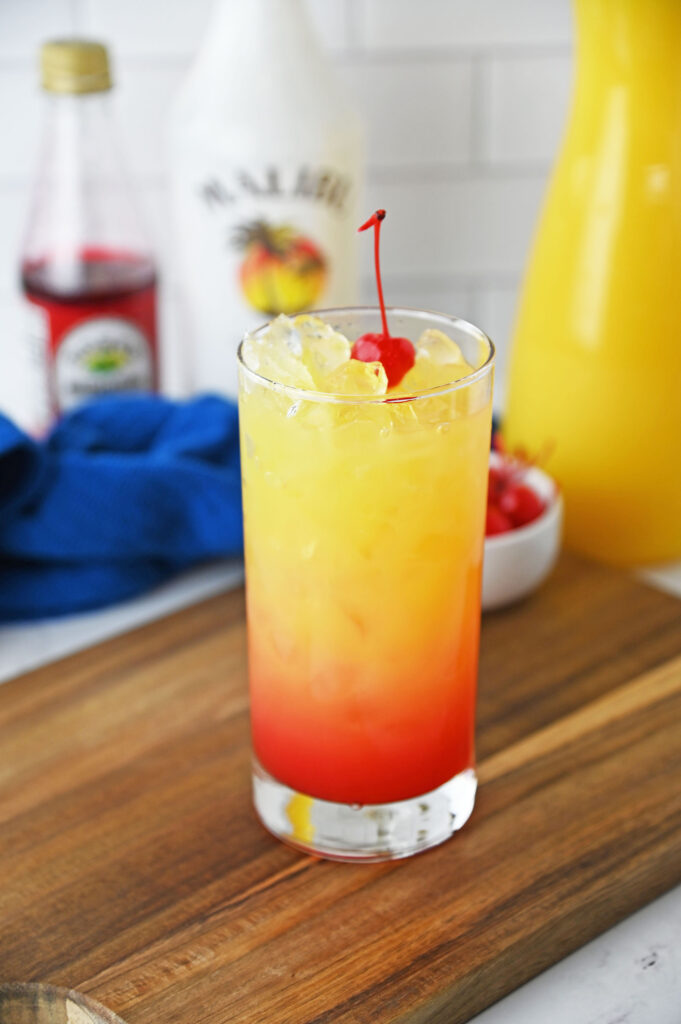 a yellow and red Malibu Rum Punch cocktail on a table, garnished with a maraschino cherry