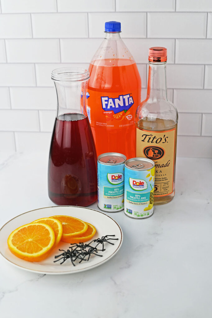 red halloween punch ingredients- fanta, cranberry juice, pineapple juice, Tito's vodka, on a counter